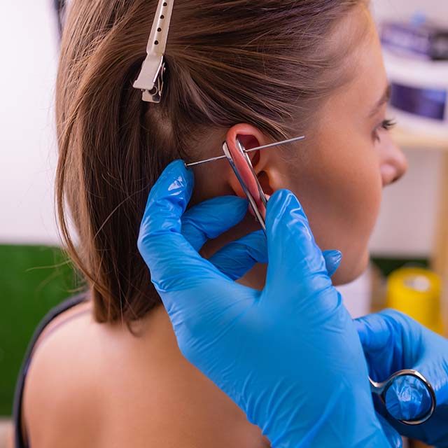 professional-holding-jewel-piercing-just-before-screw-ball__ ear piercing at a tattoo parlor
